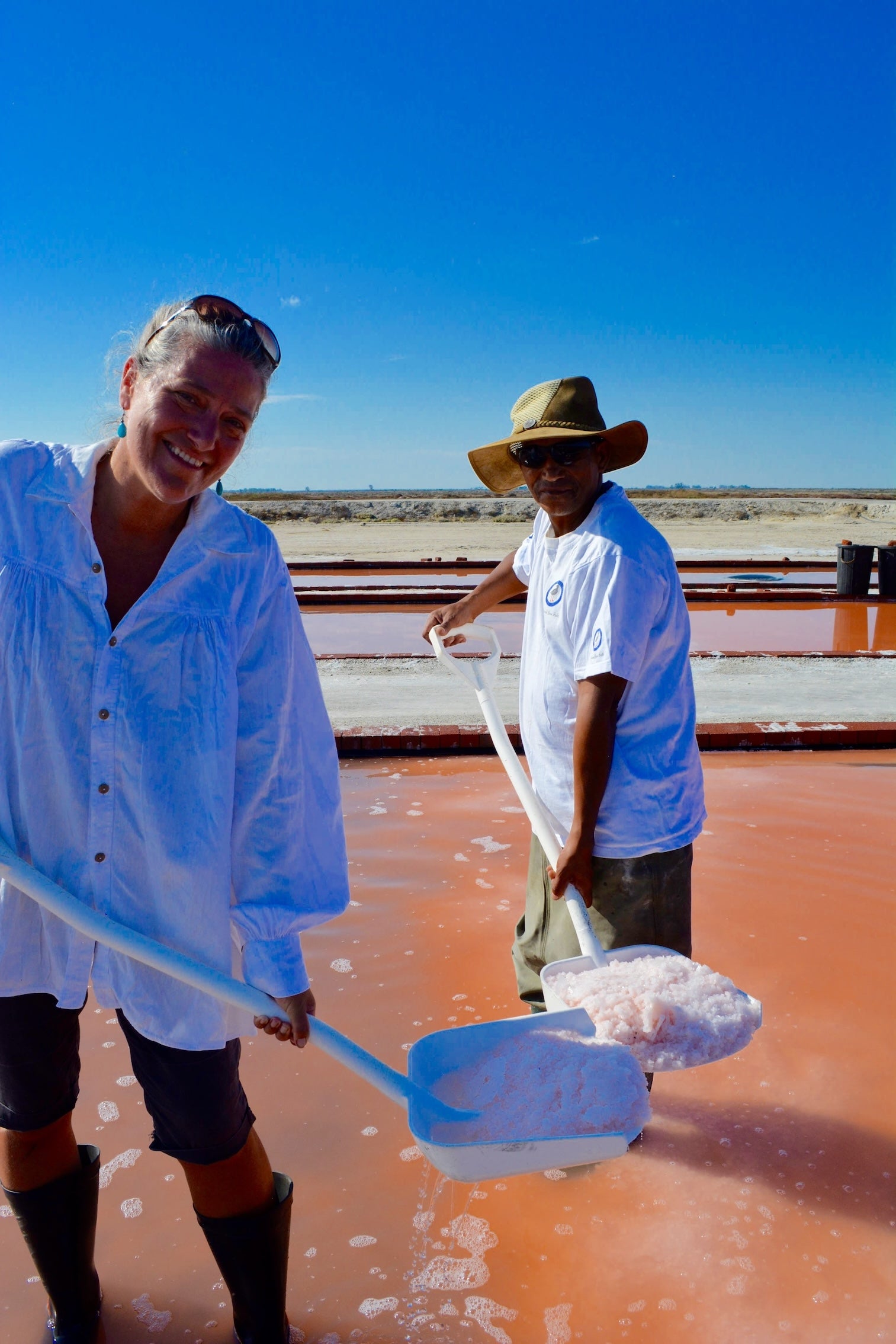 Two people in white shirts in South Africa with gleaming white sea salt in shovels
